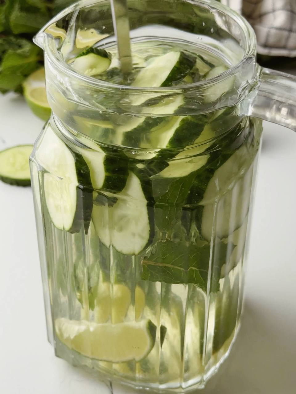 Stirring cucumber lime water in a clear glass pitcher