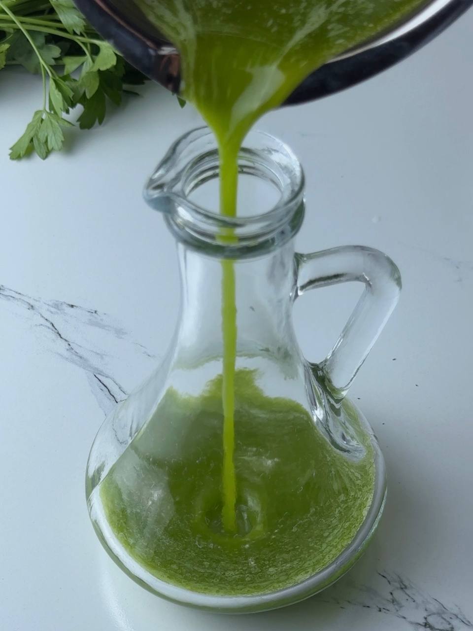 Pouring strained green herb oil into glass storage bottle