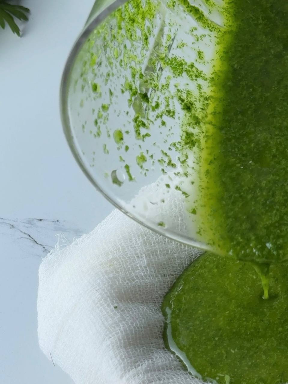 Pouring blended parsley oil through cheesecloth to strain