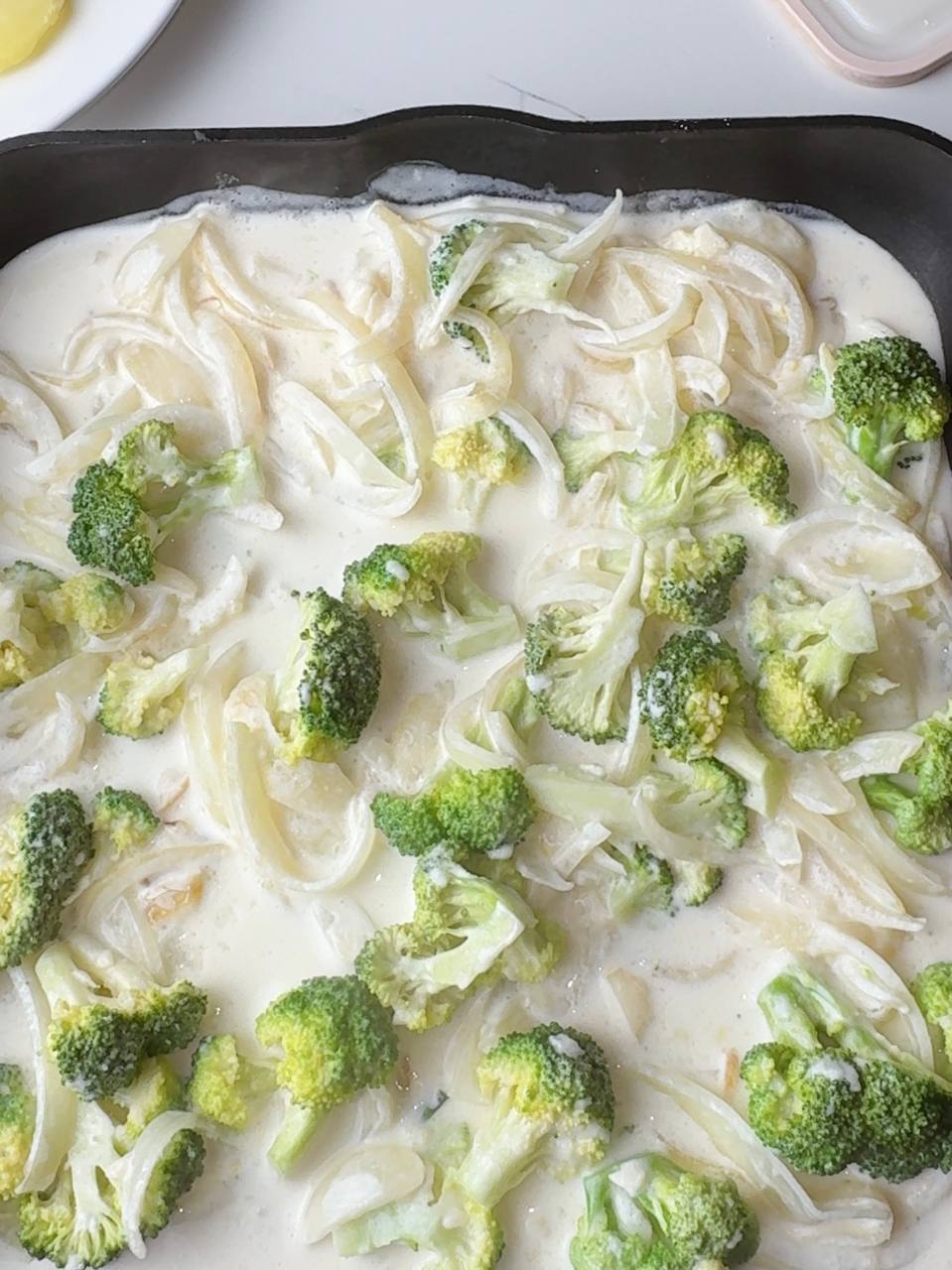 Pouring creamy broccoli sauce into the baking dish as base layer