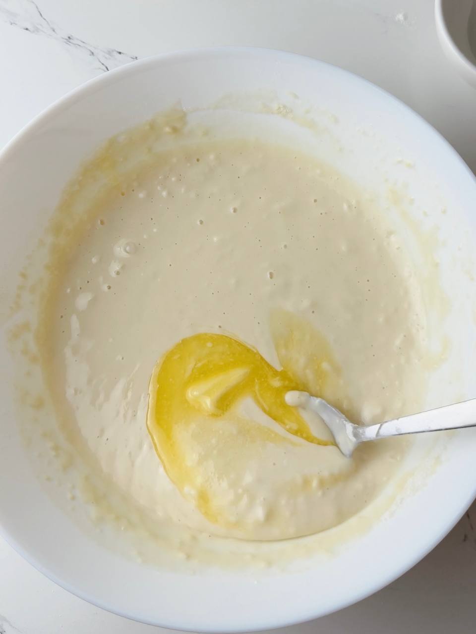 Pouring melted butter into pancake batter for rich flavor and soft texture