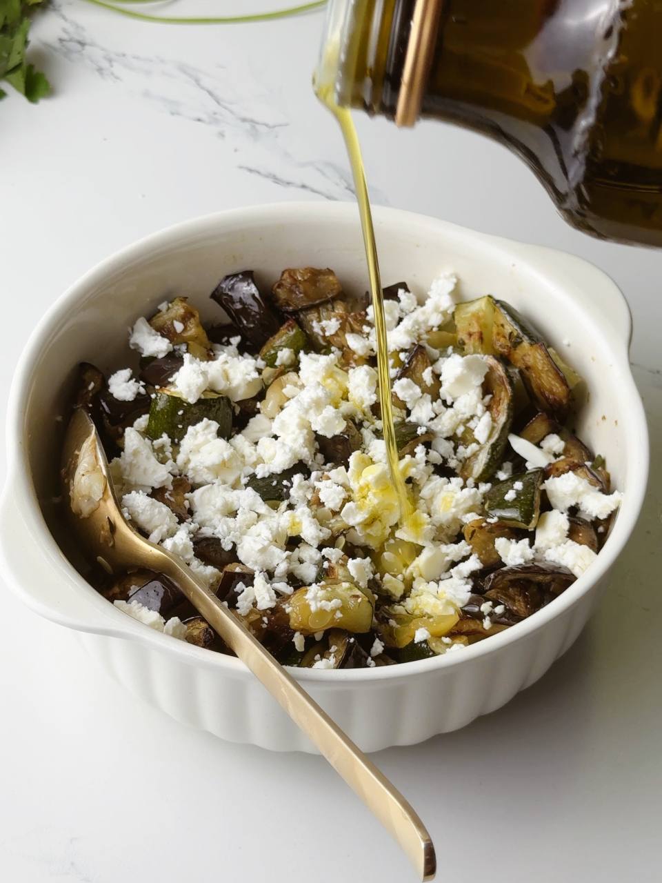 Olive oil being added to a tray of freshly baked Mediterranean vegetables with feta