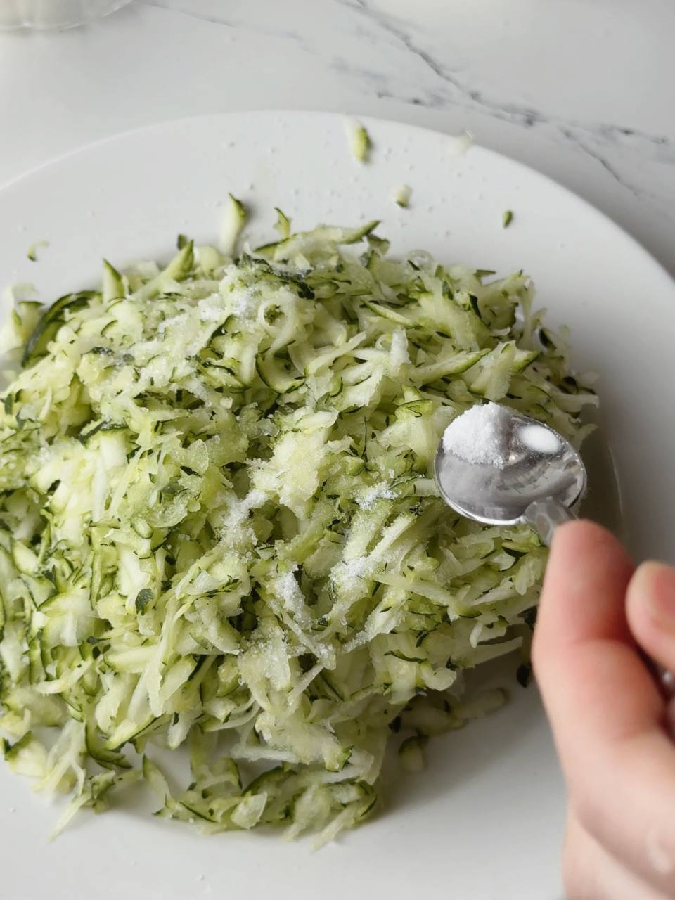 Salt being added to grated zucchini to draw out excess moisture