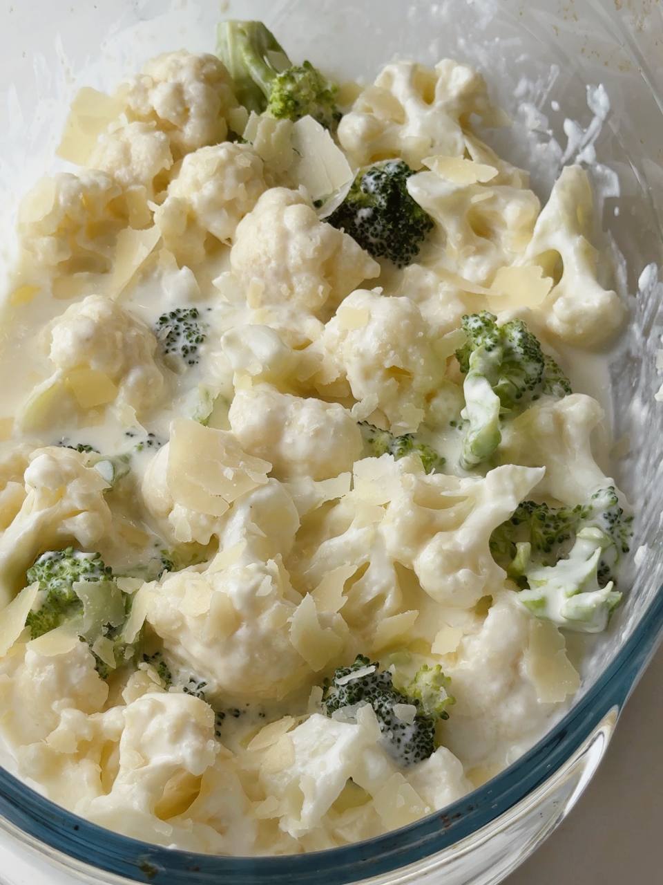 Blanched vegetables in baking dish being topped with cheese sauce.