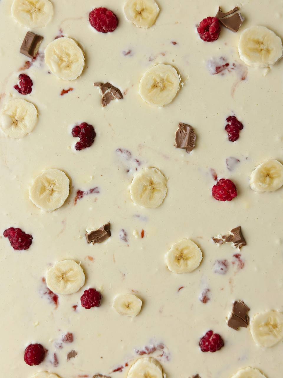 Unbaked banana pancake topped with sliced banana, raspberries, strawberry jam, and chocolate