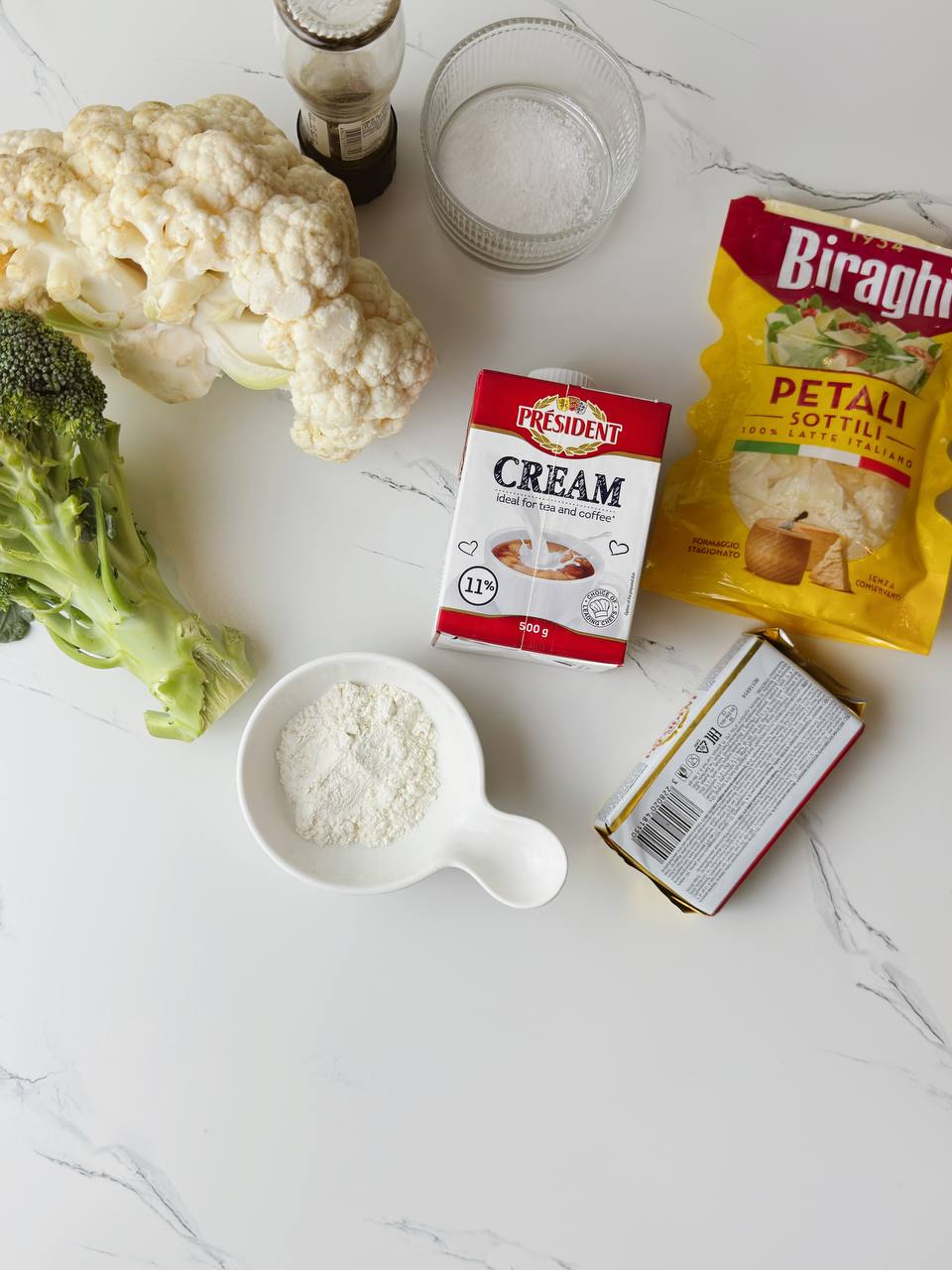 Ingredients for broccoli and cauliflower gratin including cream, cheese, and vegetables.