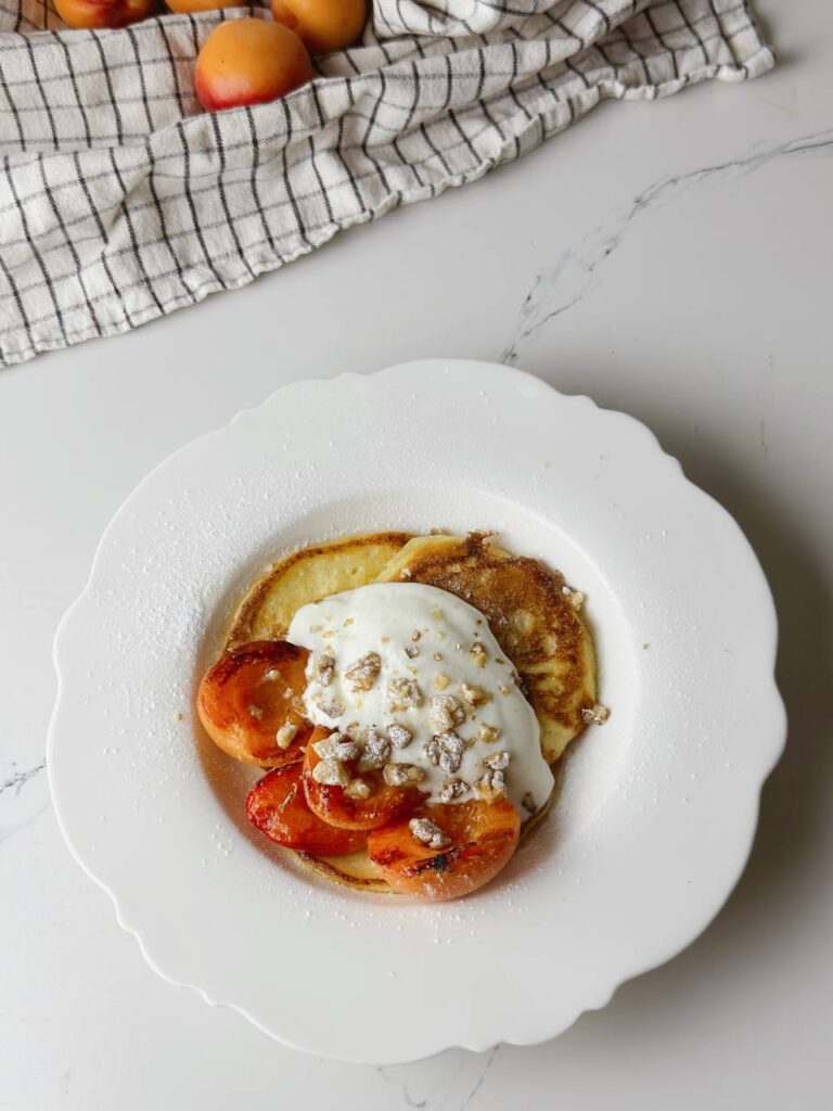 Top view of a breakfast plate with cottage cheese pancakes and grilled apricots.