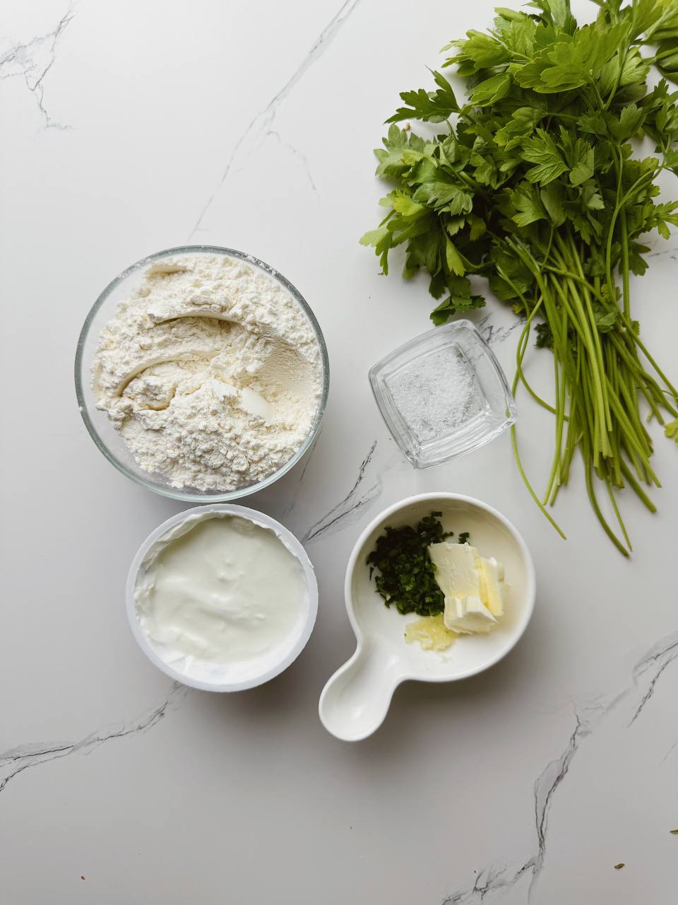 Ingredients for garlic flatbread in a pan, including flour, yogurt, baking powder, salt, butter, garlic, and parsley.