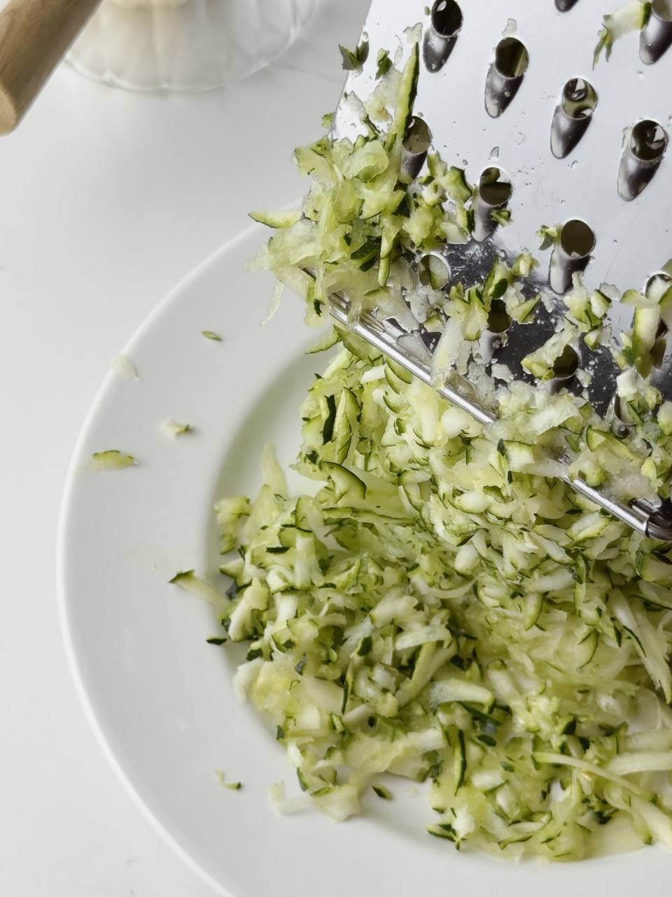 Fresh zucchini being grated on a box grater for waffle batter