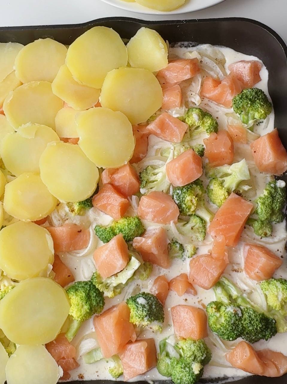 Adding seasoned salmon and layering potato slices on top