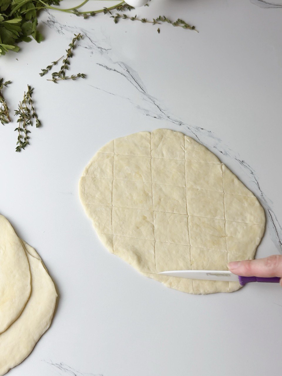 Criss-cross pattern being scored into flatbread dough with a knife.