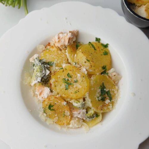 Plated serving of creamy baked salmon with potato and broccoli, topped with Biraghi cheese