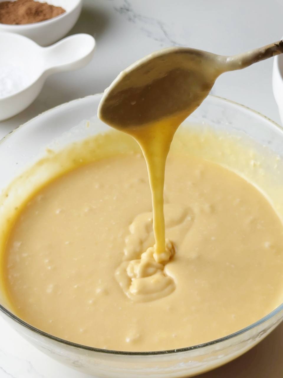 A spoon lifting smooth condensed milk batter to show the texture.