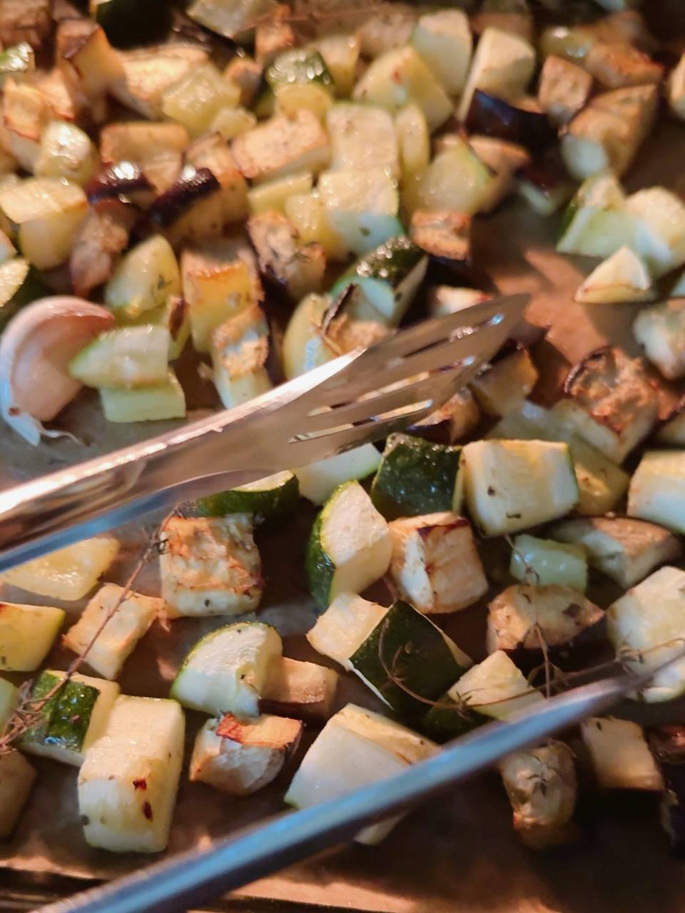 Roasted vegetables being stirred halfway through baking for even cooking and caramelization.