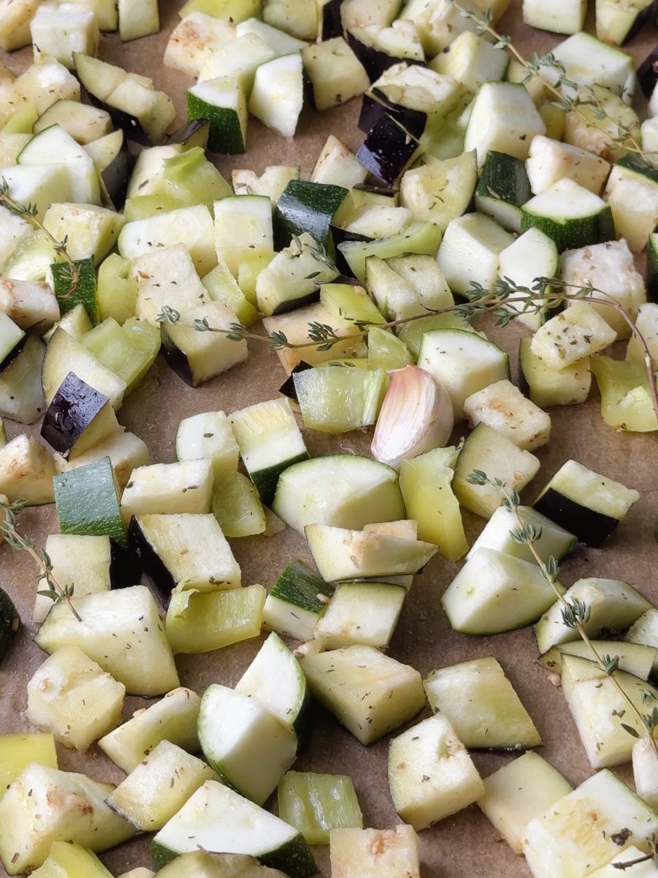 ucchini, eggplant, and bell pepper tossed with herbs and garlic on a tray before baking.