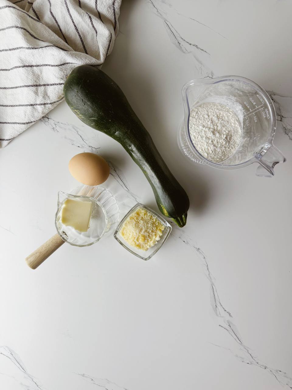 Ingredients for zucchini waffles with parmesan, including grated zucchini, egg, flour, butter, and Parmesan cheese
