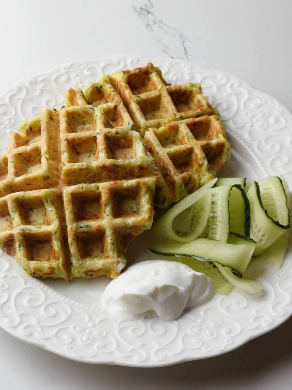 Crispy zucchini waffle served with Greek yogurt and cucumber slices on the side