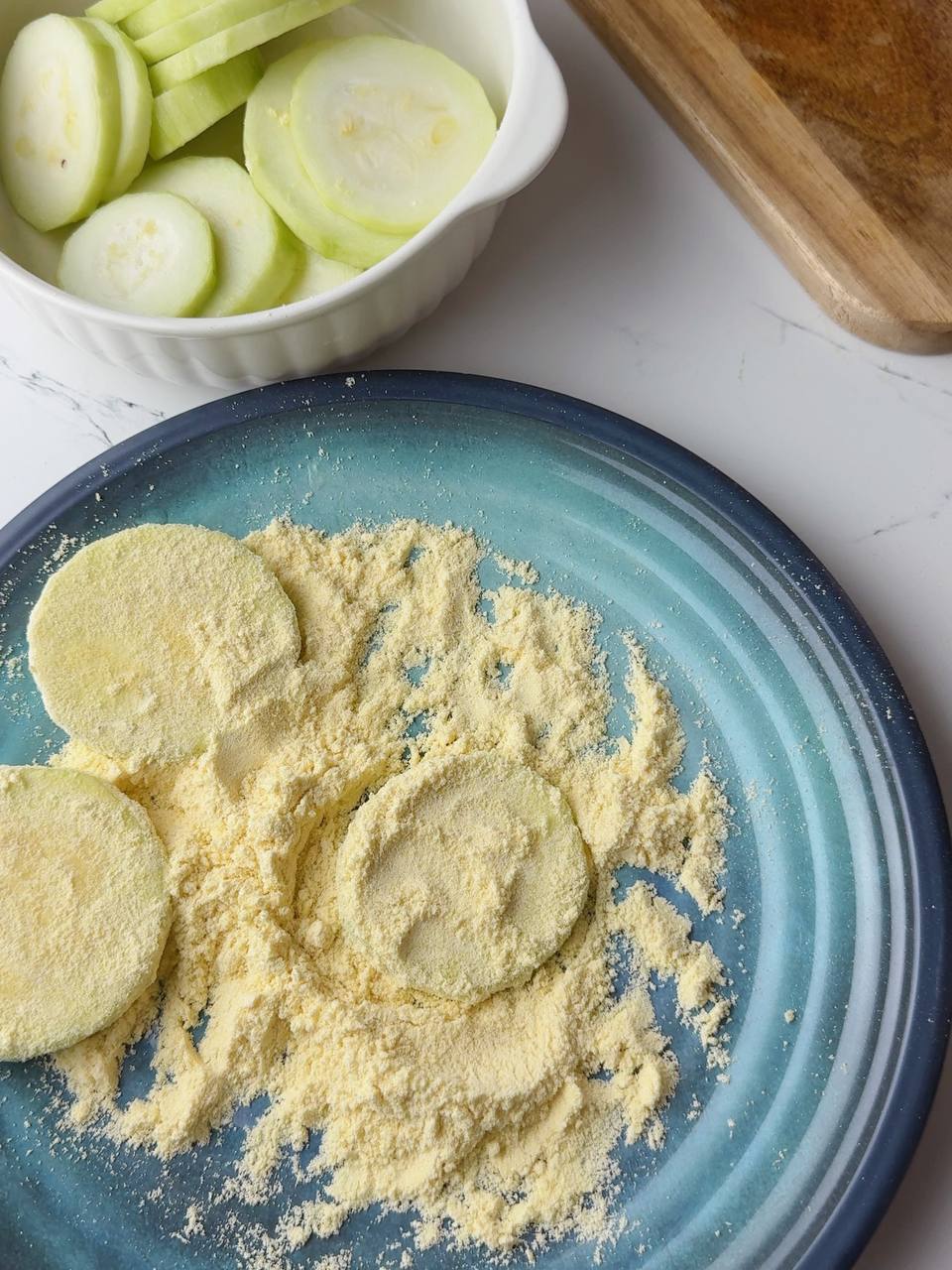Hand coating salted zucchini slices in seasoned corn flour mixture.