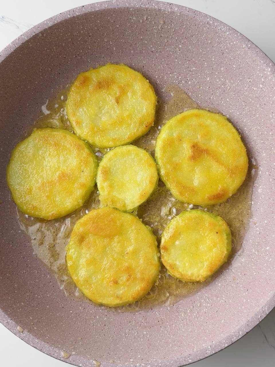 Crispy golden zucchini rounds flipped and frying to perfection.