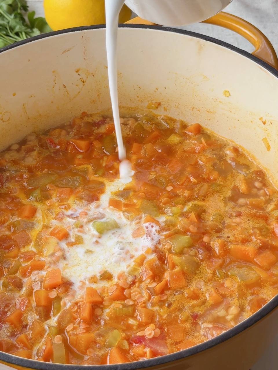 Pouring creamy coconut milk into red lentil soup for rich flavor.