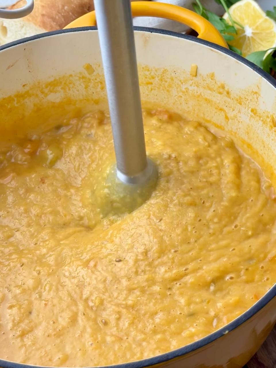 Blending red lentil soup with a hand blender until smooth and creamy.