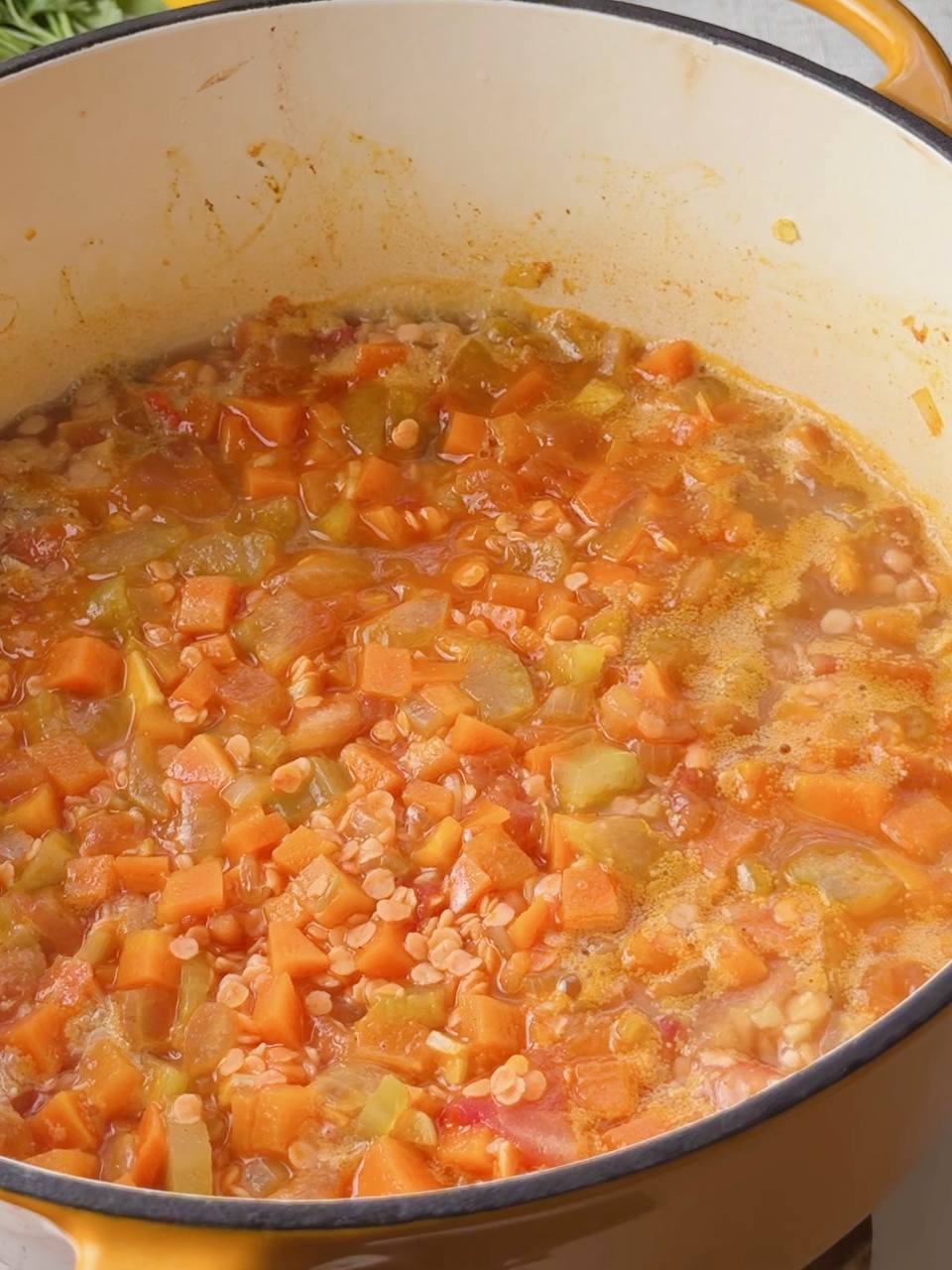 Pot of red lentil soup with added spices and vegetable broth simmering on the stove.