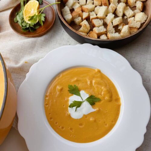 Bowl of creamy red lentil soup served with Greek yogurt, fresh parsley, and crunchy croutons.
