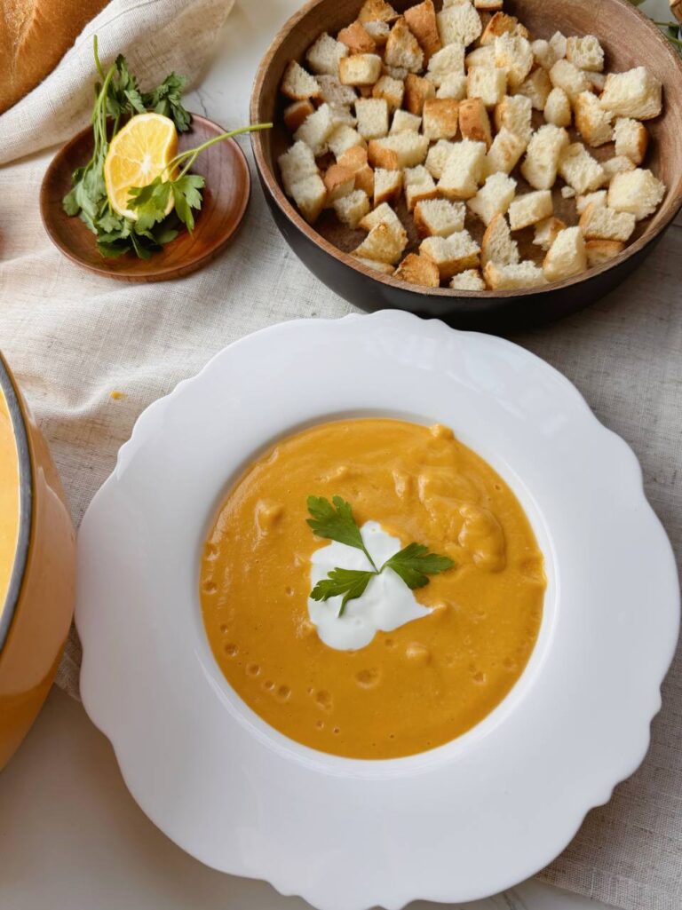 Bowl of creamy red lentil soup served with Greek yogurt, fresh parsley, and crunchy croutons.