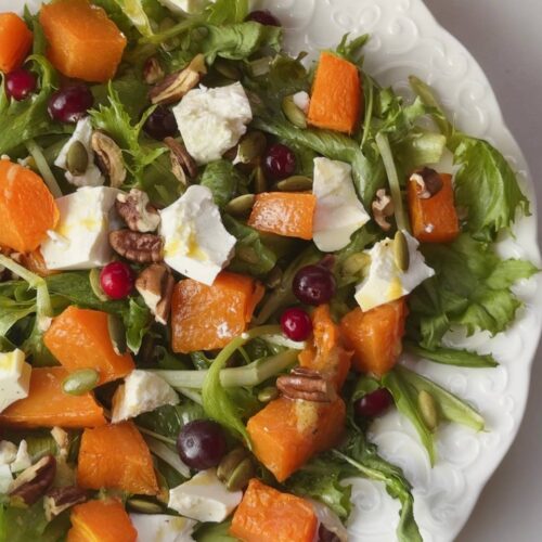 Baked pumpkin salad with toasted pecans, pumpkin seeds, and frozen cranberries ready to serve