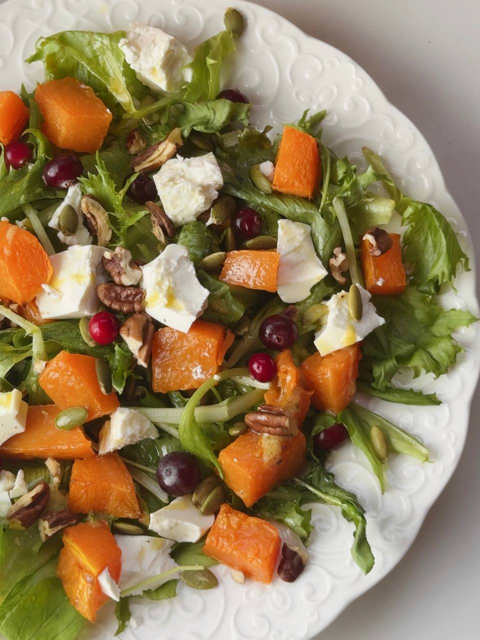 Baked pumpkin salad with toasted pecans, pumpkin seeds, and frozen cranberries ready to serve