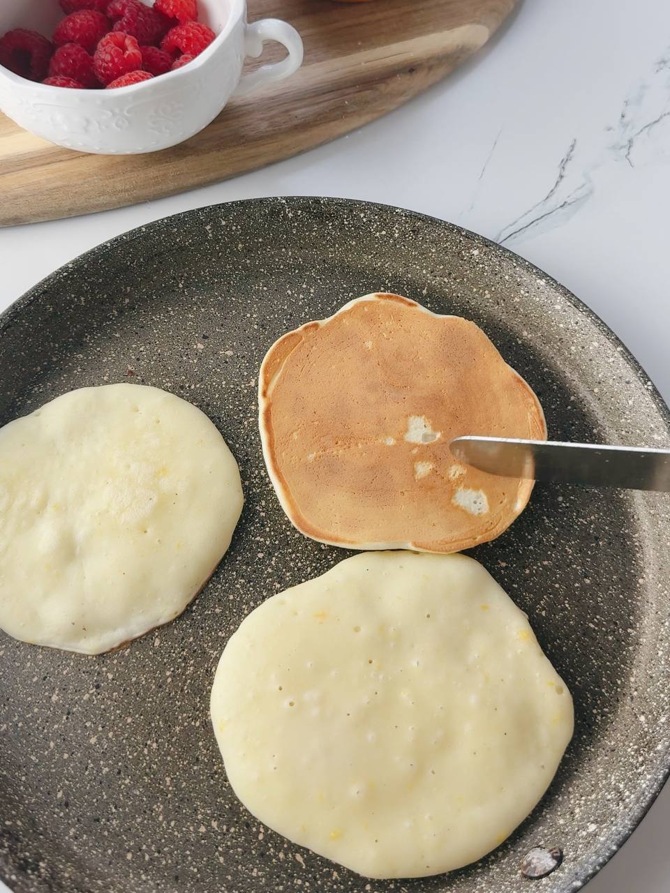 Lemon yogurt pancakes cooking on a pan with bubbles on the surface