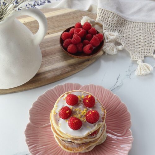 Lemon yogurt pancakes with raspberries, lemon zest, and creamy yogurt topping, fresh raspberries in the background