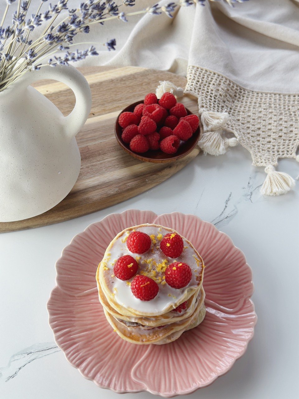 Lemon yogurt pancakes with raspberries, lemon zest, and creamy yogurt topping, fresh raspberries in the background