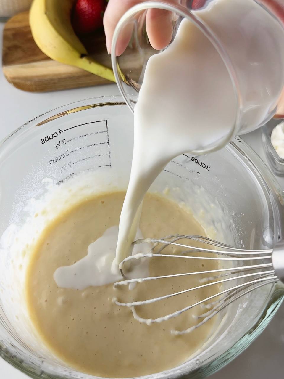 Pouring milk into pancake batter and mixing until smooth