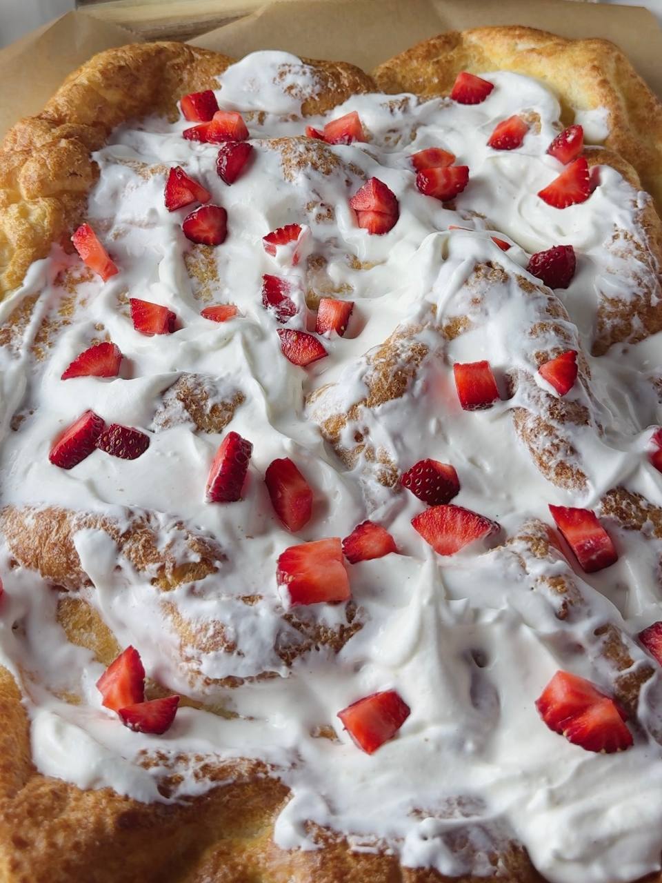 Spreading cream and fresh strawberries on baked pancake