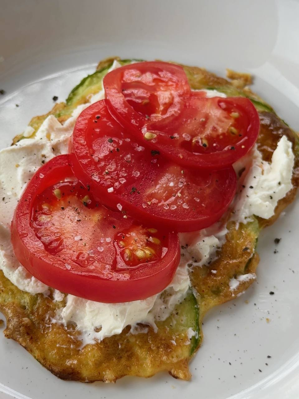 cream cheese and sliced tomato on baked zucchini layer