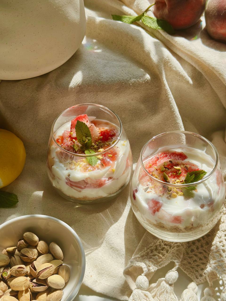 two no-bake peach cheesecake cups served with fresh peaches and pistachios