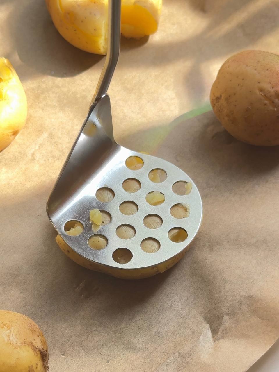gently smashing boiled potatoes on a parchment-lined baking tray