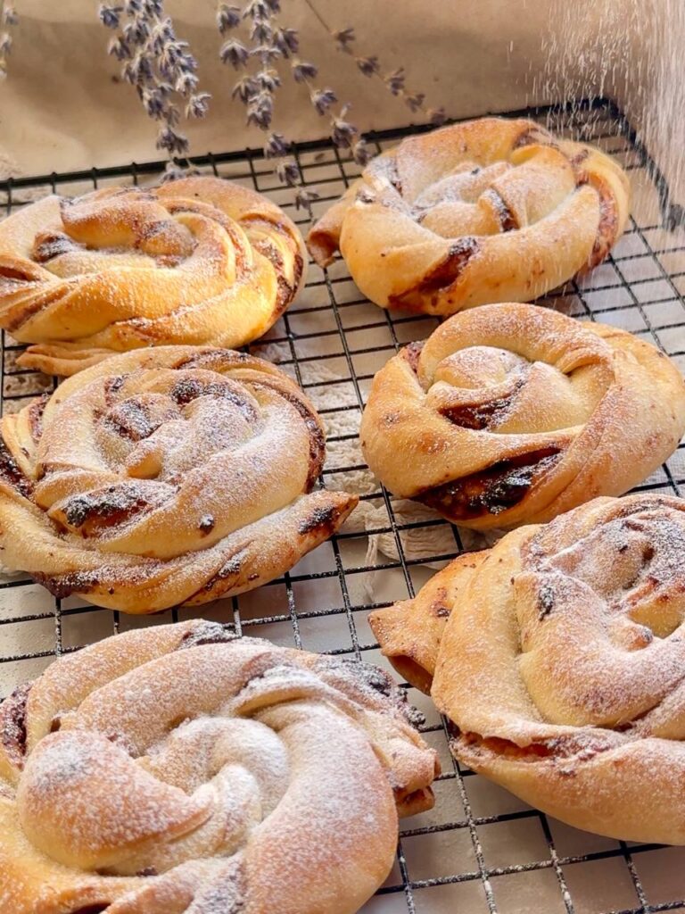 Freshly baked flaky cottage cheese buns with blackcurrant jam cooling on a wire rack