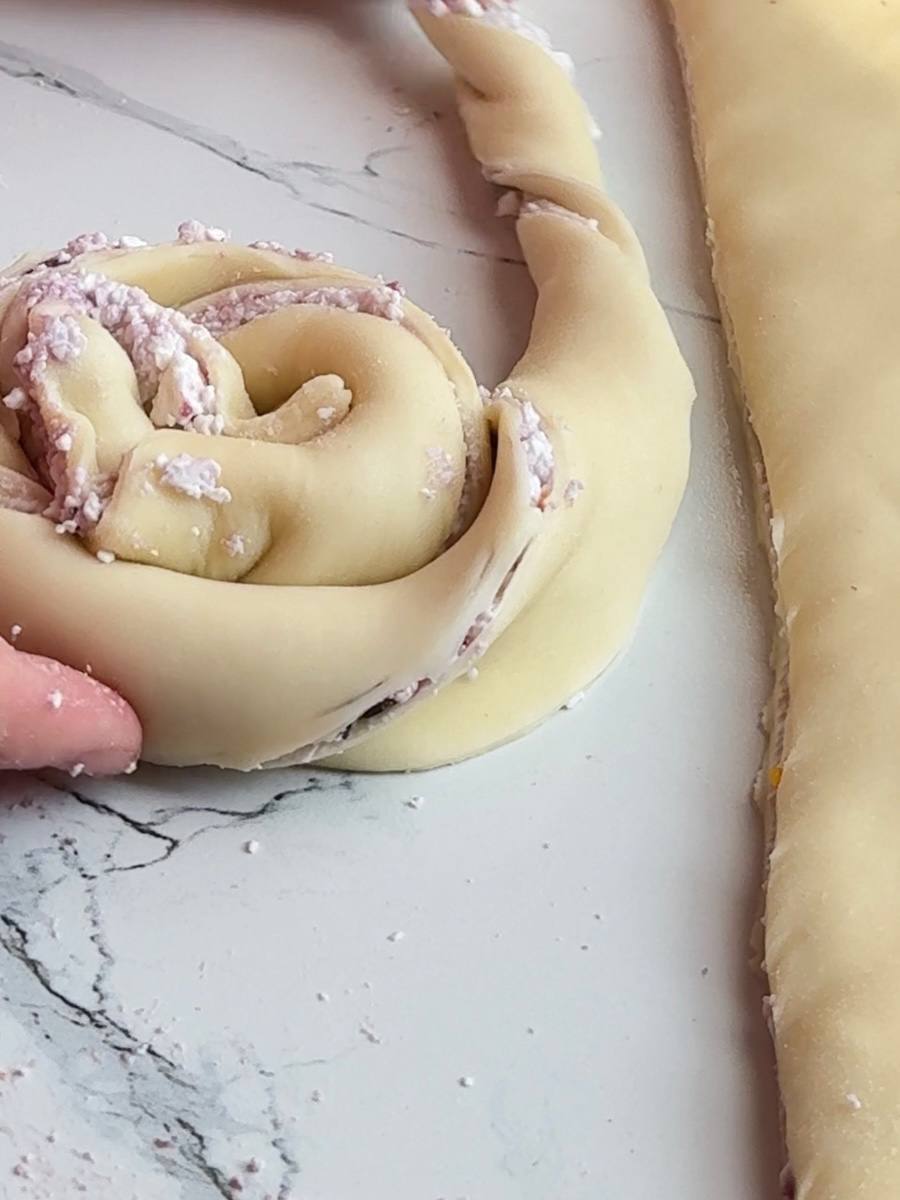 Twisted puff pastry strip being shaped into a round cottage cheese bun