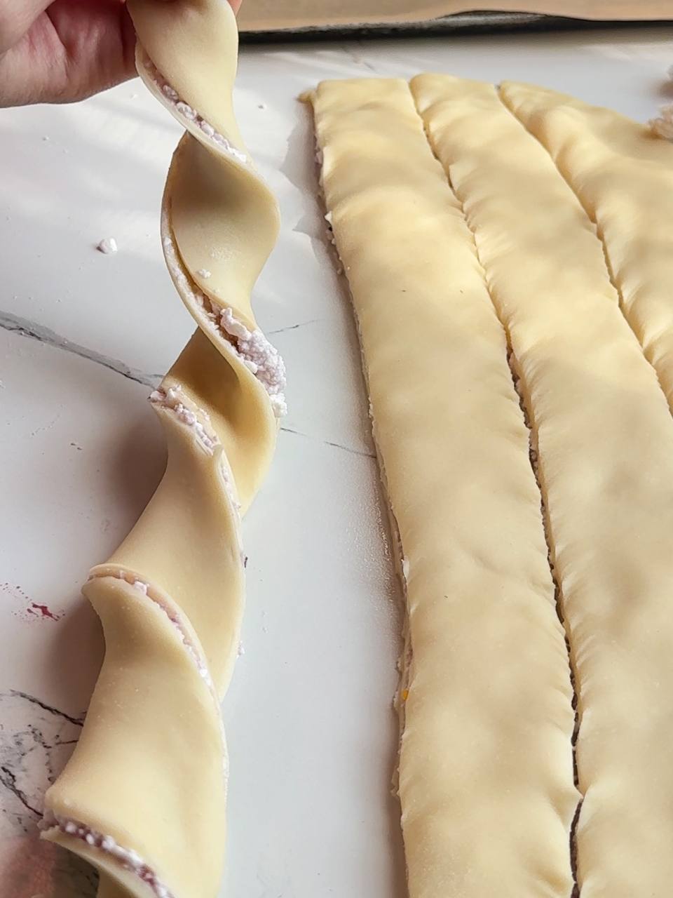Twisting a filled puff pastry strip to shape the cottage cheese bun