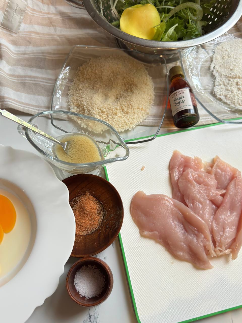 Ingredients for chicken with panko breading, including chicken breast, breadcrumbs, flour, eggs, seasonings, and fresh salad greens.