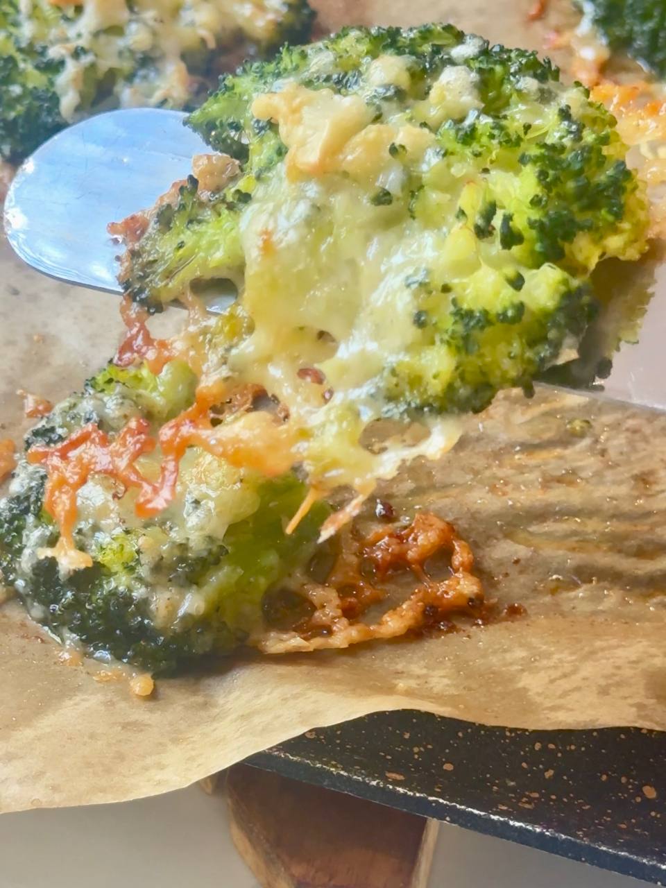 Close-up of crispy Parmesan broccoli being lifted from the baking sheet with a spatula.