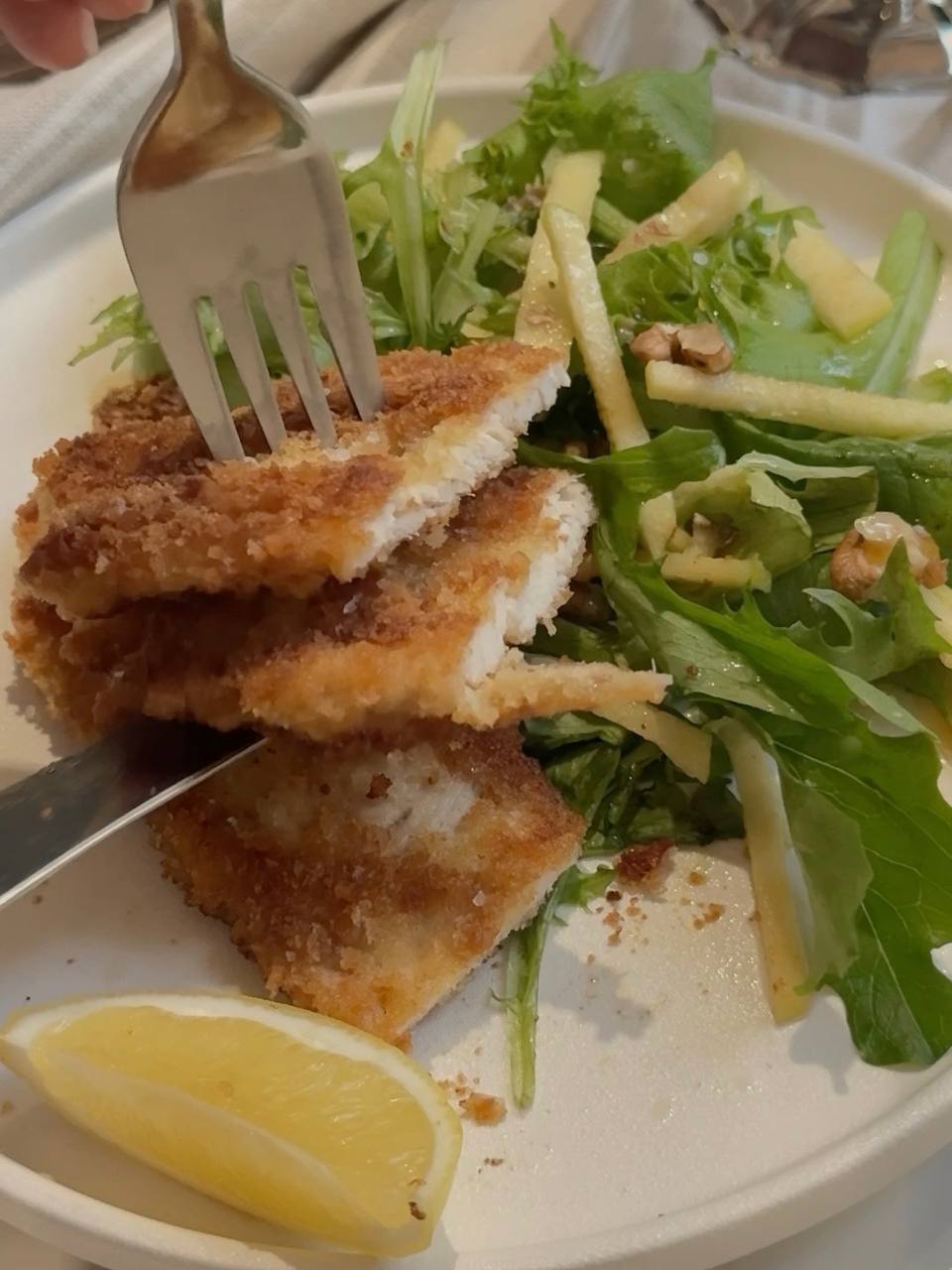 Close-up of crispy panko chicken schnitzel cut open to reveal tender white chicken, served with green apple and walnut salad.