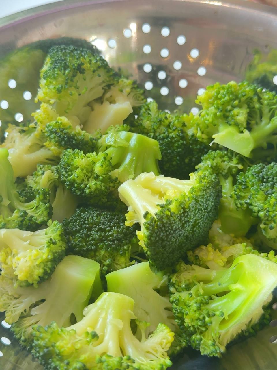 Cooked broccoli florets draining in a colander after boiling.