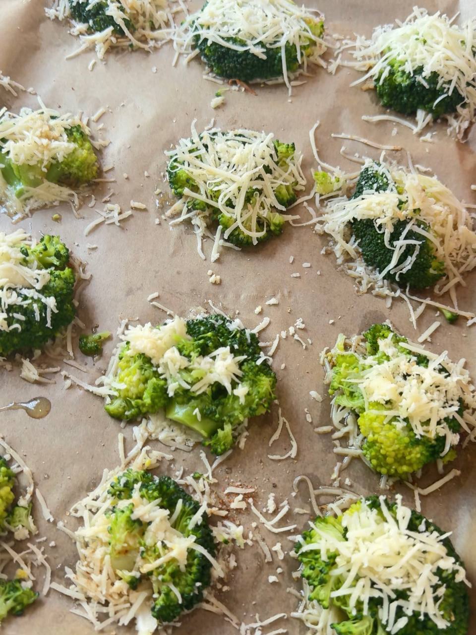 Smashed broccoli with garlic and Parmesan arranged on a parchment-lined baking sheet.