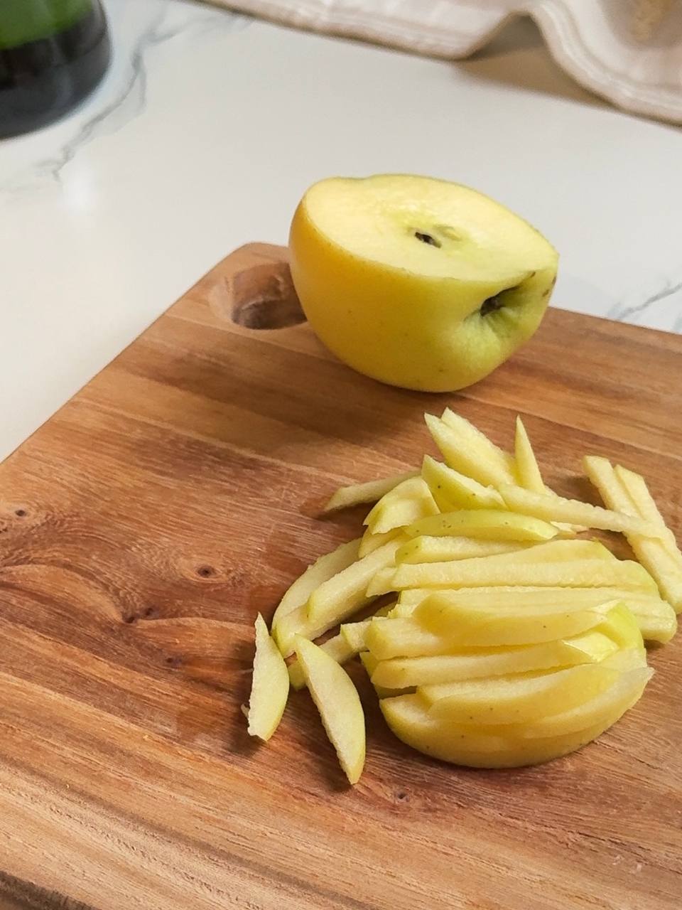 Fresh green apple cut into thin matchsticks on a wooden cutting board for a crisp apple salad.