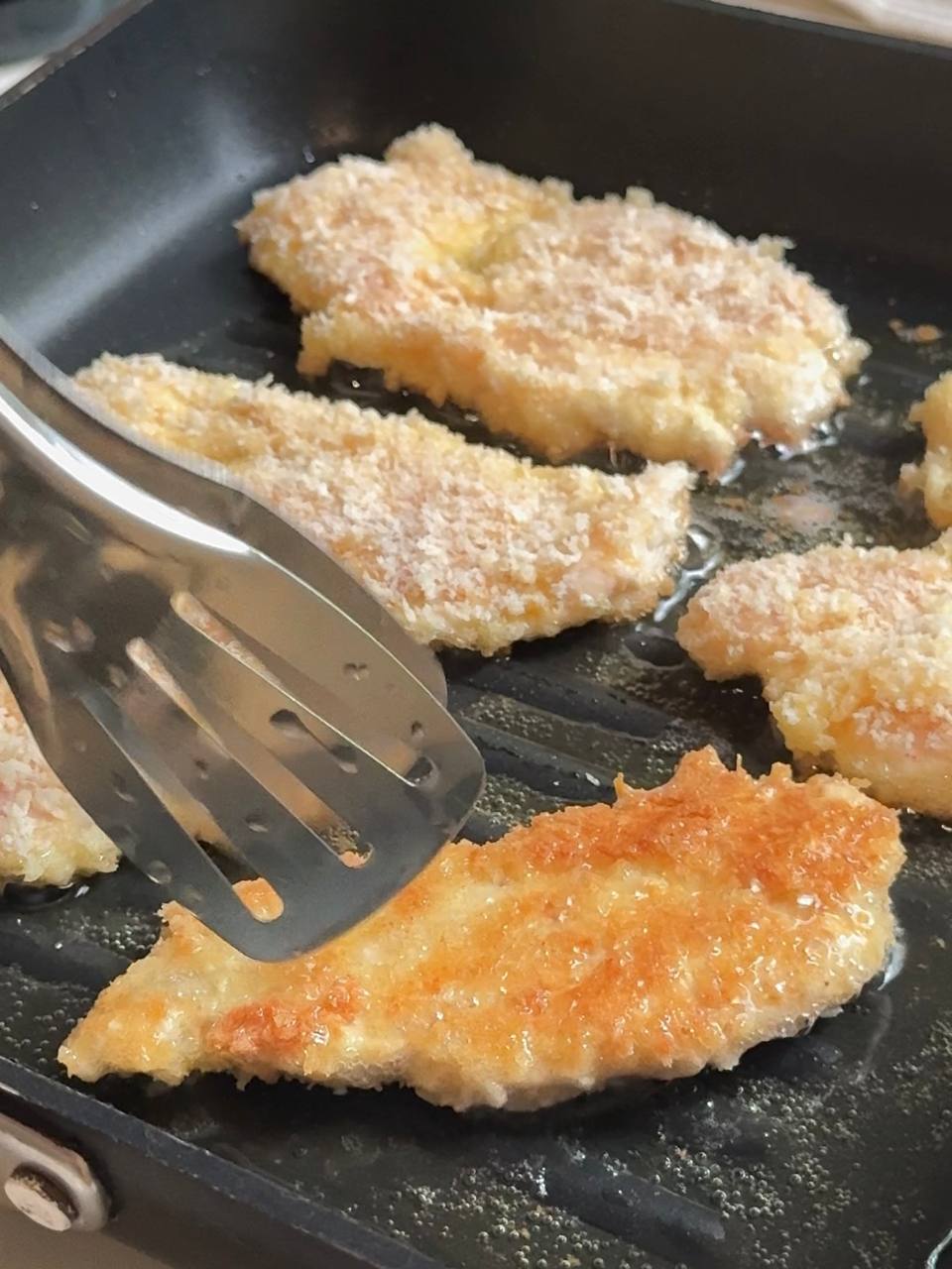 Chicken with panko breading frying in olive oil in a skillet until golden brown and crispy.