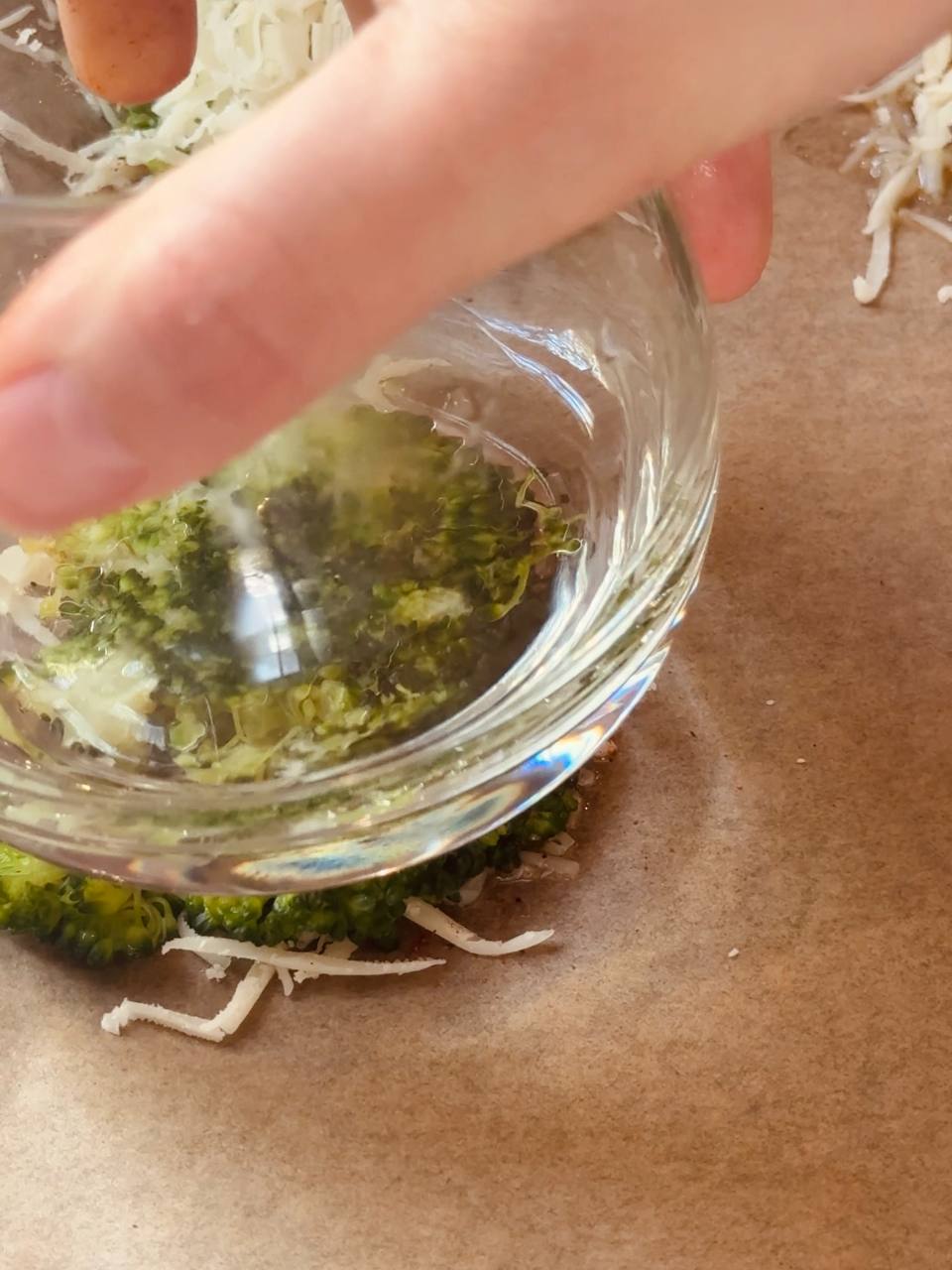 Cooked broccoli being gently smashed with the bottom of a glass.
